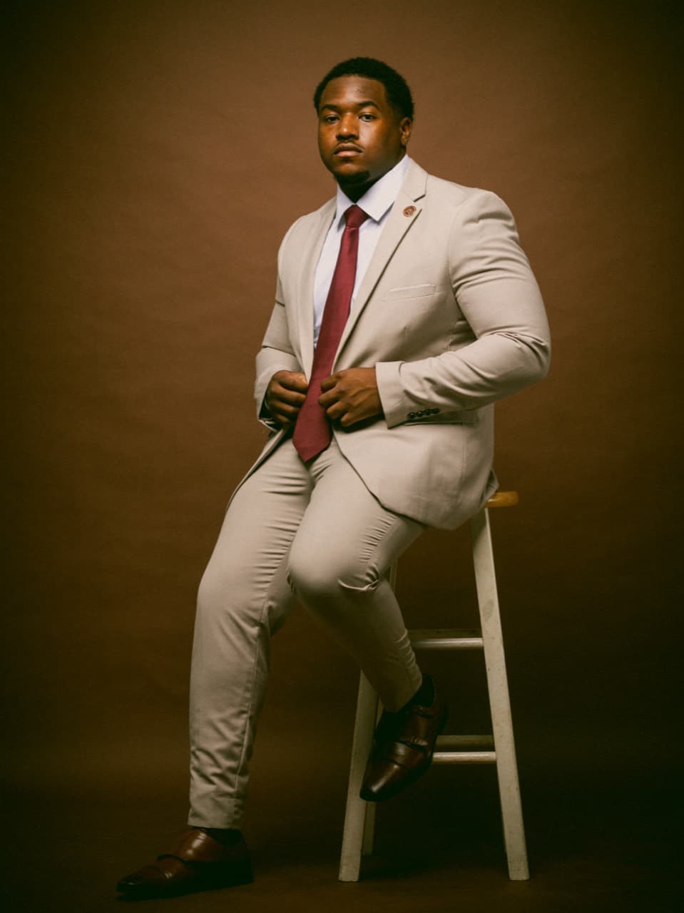 Studio portrait of a man in a beige suit seated on a stool