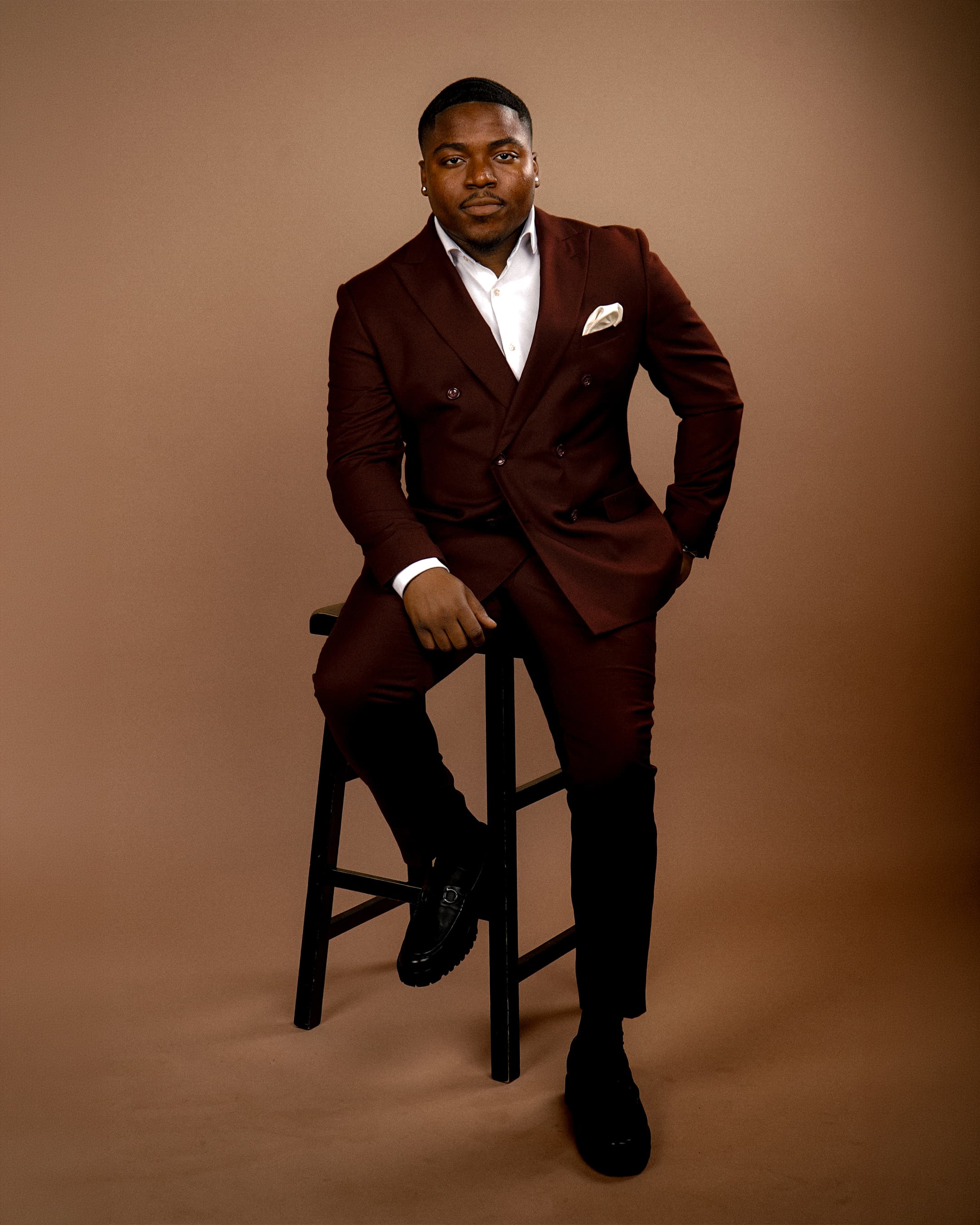 Studio portrait of a man in a brown suit seated on a stool